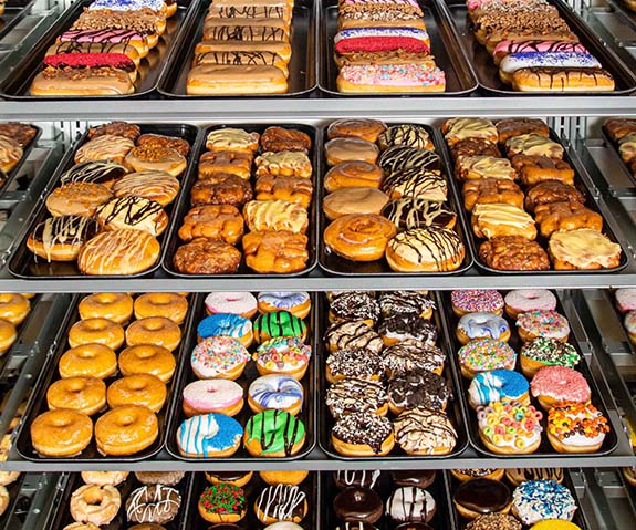 Large donut case filled with an assortment of Long John donuts and round donuts in various colorful glazes